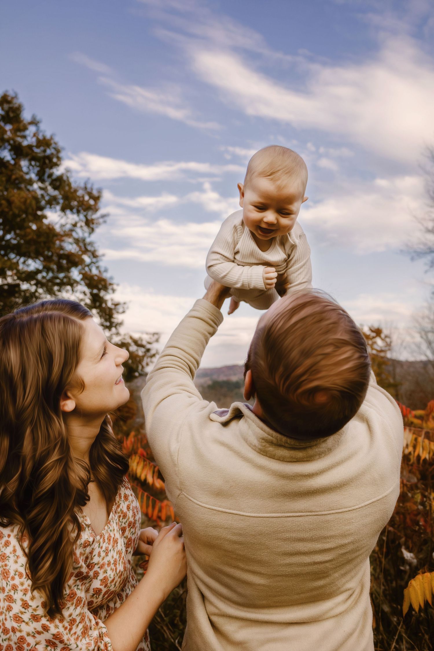 A joyful moment captured outdoors as a baby is lifted high into the air against a blue sky background.