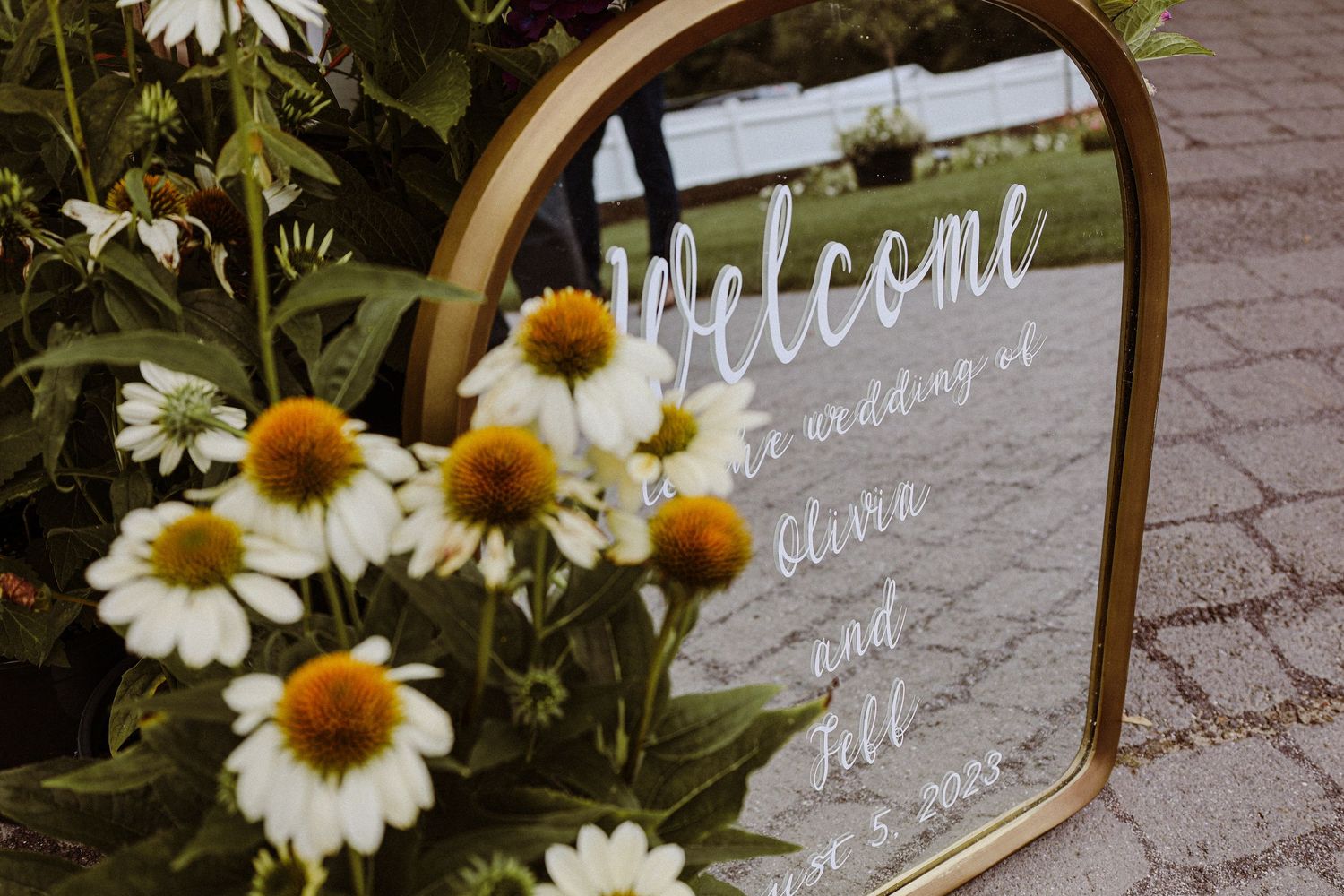 Wedding welcome sign decorated with white and yellow daisies in a golden frame.