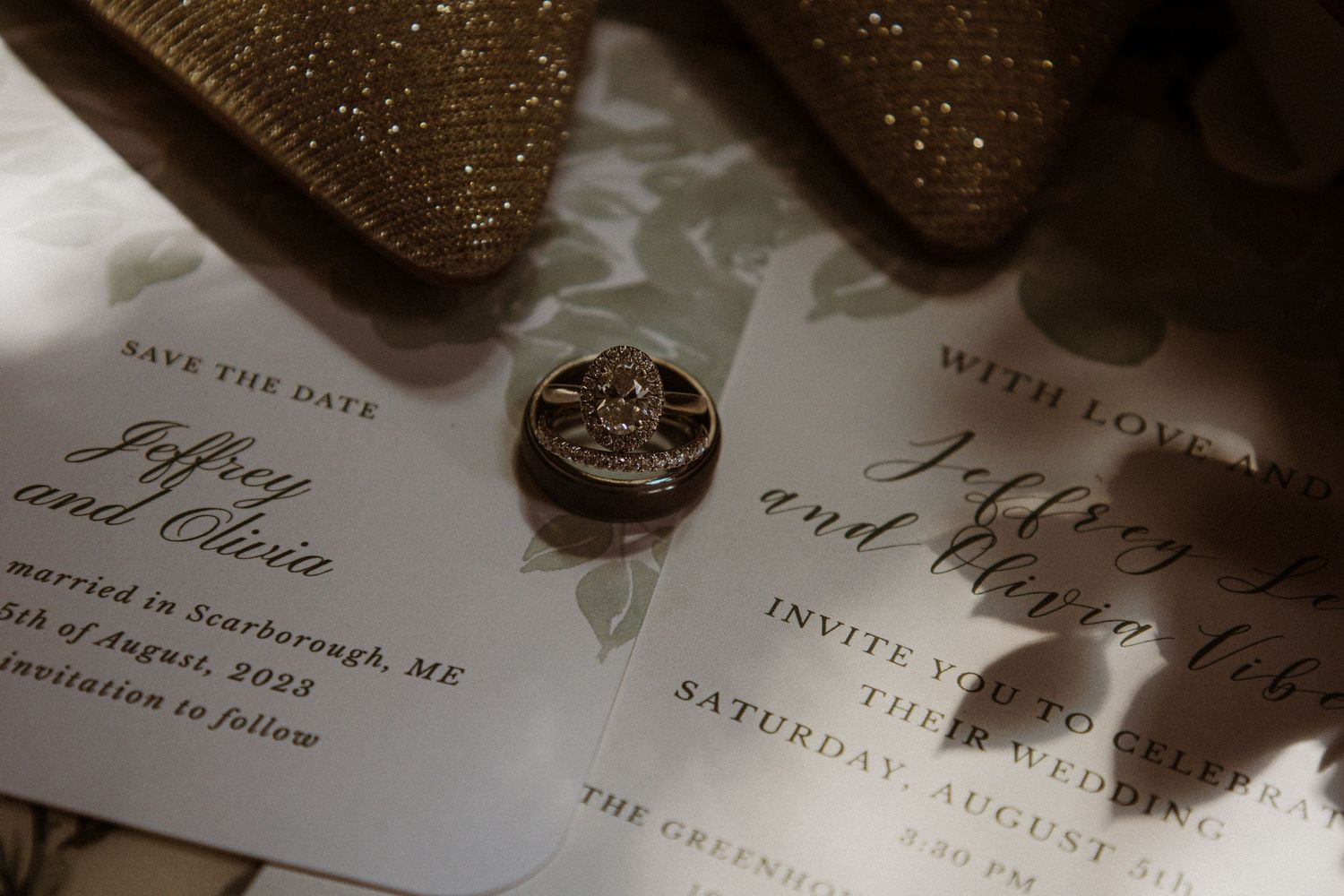 Wedding invitation and rings photographed in a moody lighting setup on a white surface.
