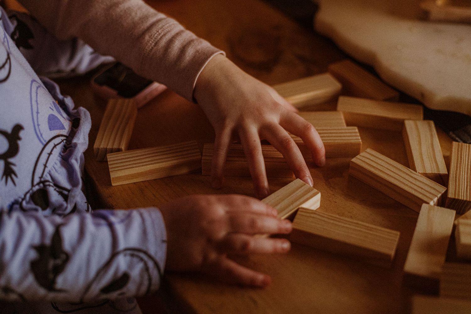 Child's hands playing with plain wooden building blocks in warm natural light.