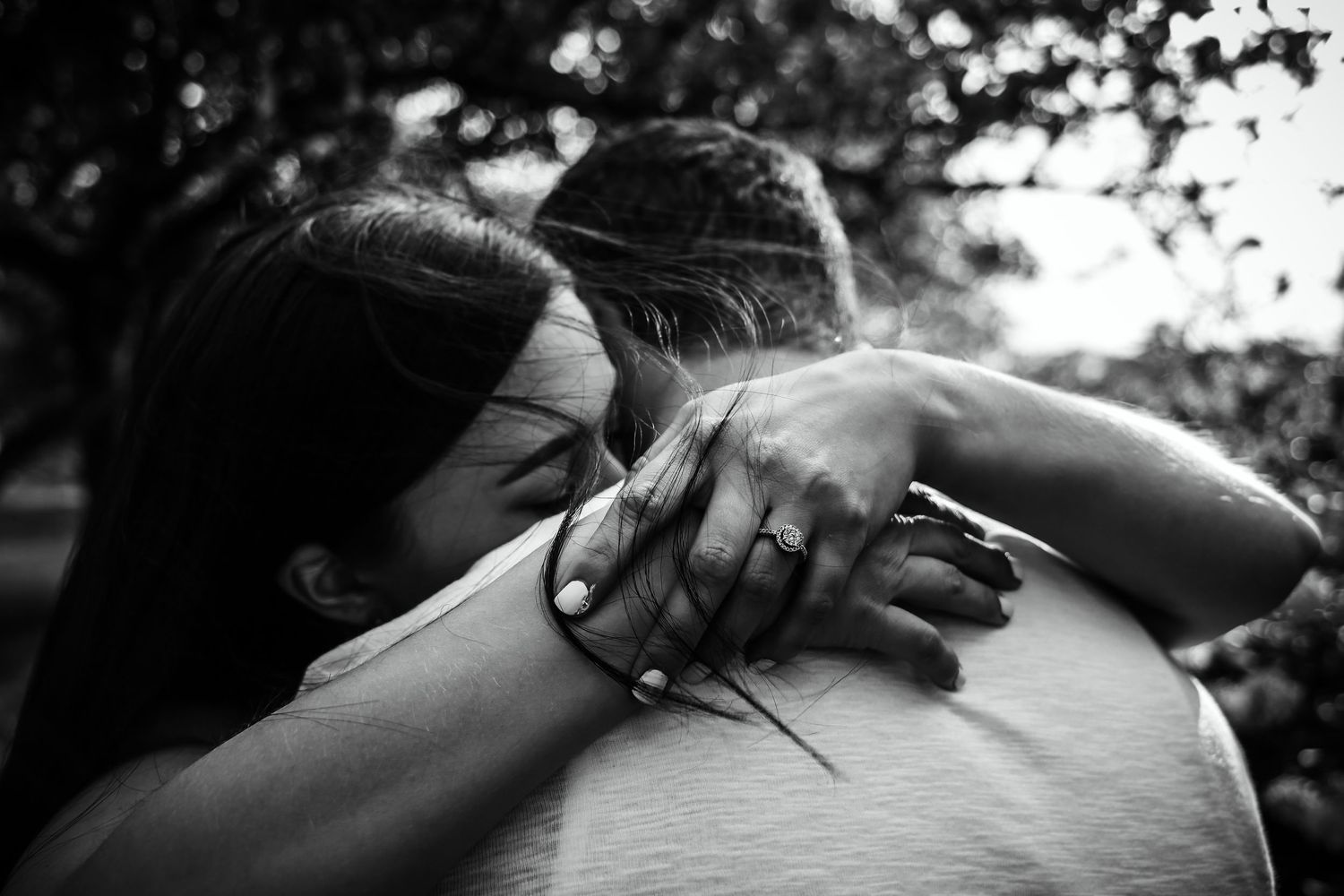 Black and white intimate embrace showing wedding rings in natural outdoor setting.