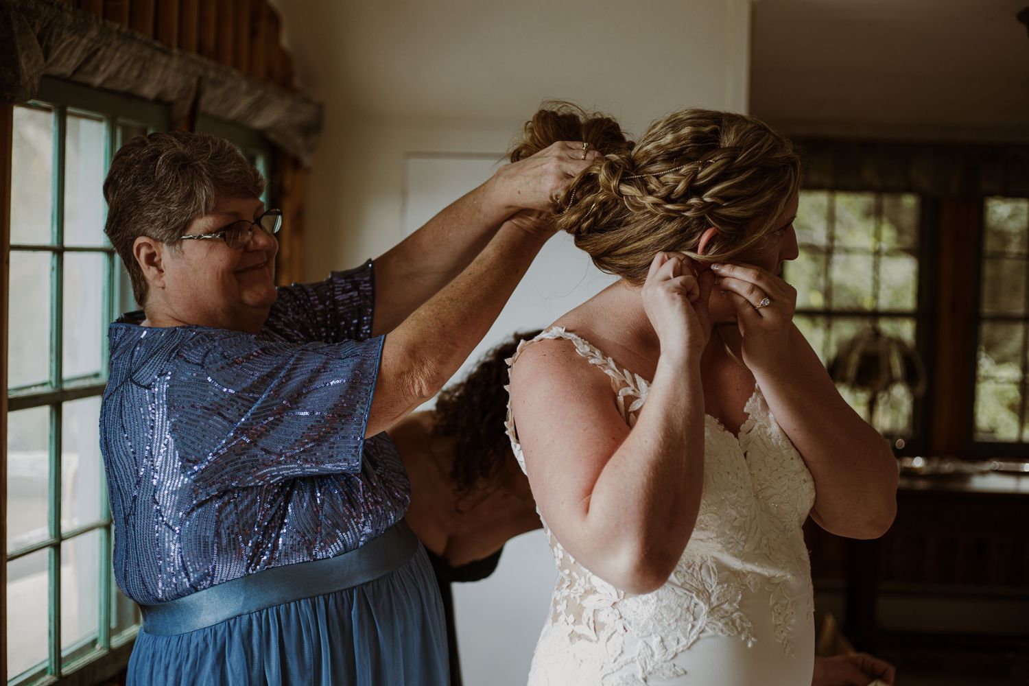 A wedding preparation moment showing final dress adjustments near a window.