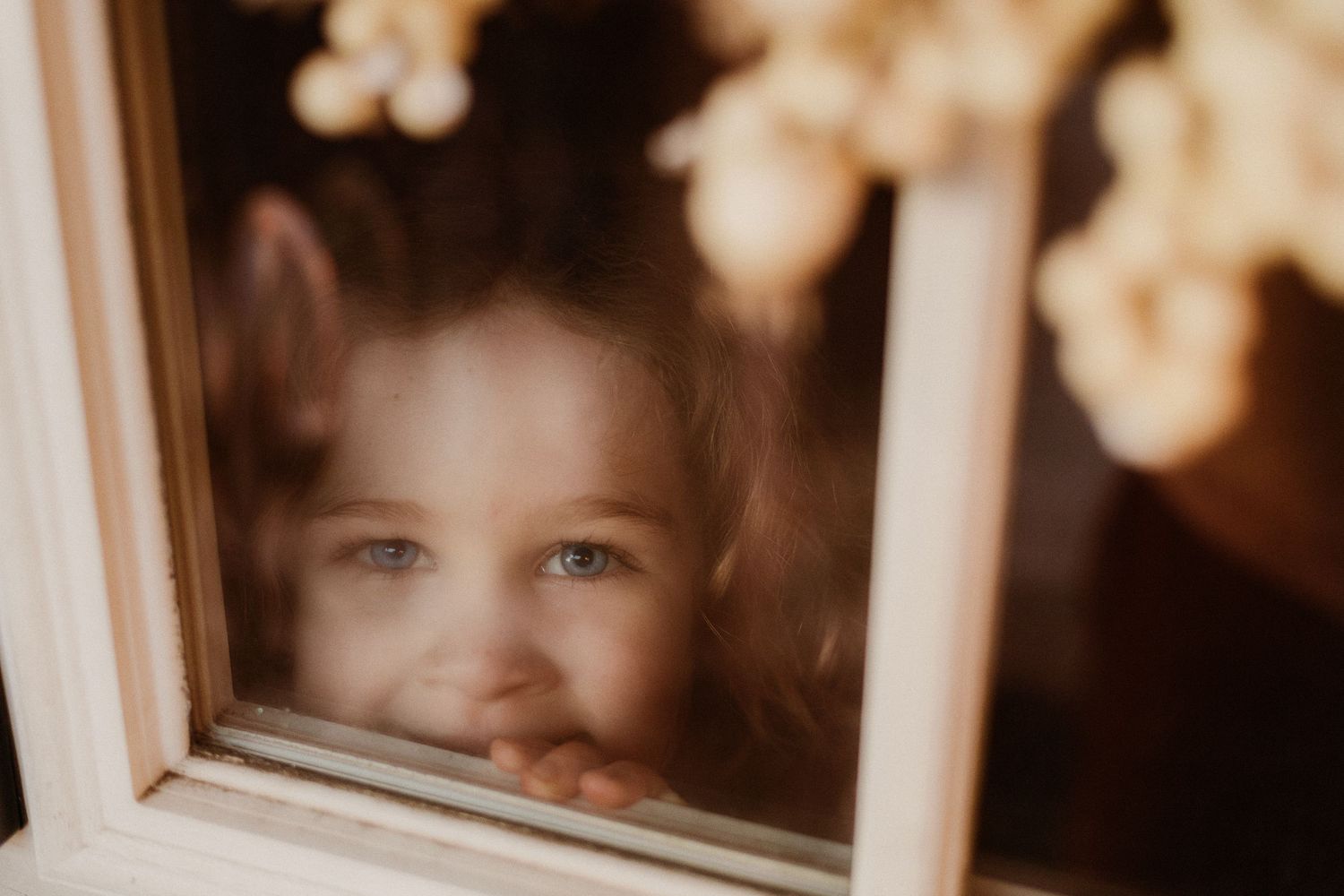 A child peers through a window with a warm sepia-toned glow, creating a nostalgic and dreamy atmosphere.