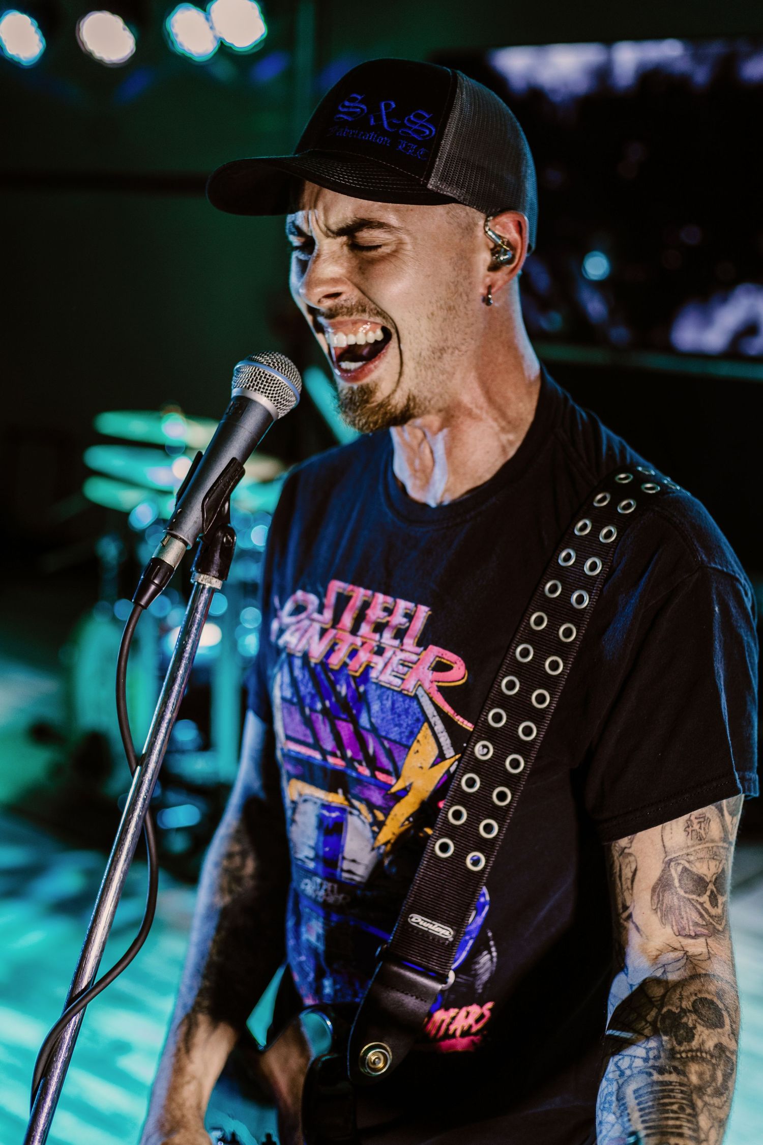 Energetic performer singing into microphone on stage with colorful blue lighting.