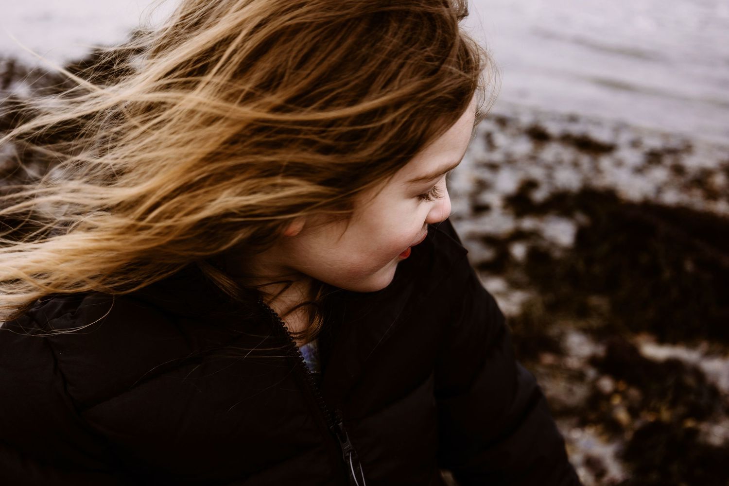 Side profile of windswept hair against moody coastal background.