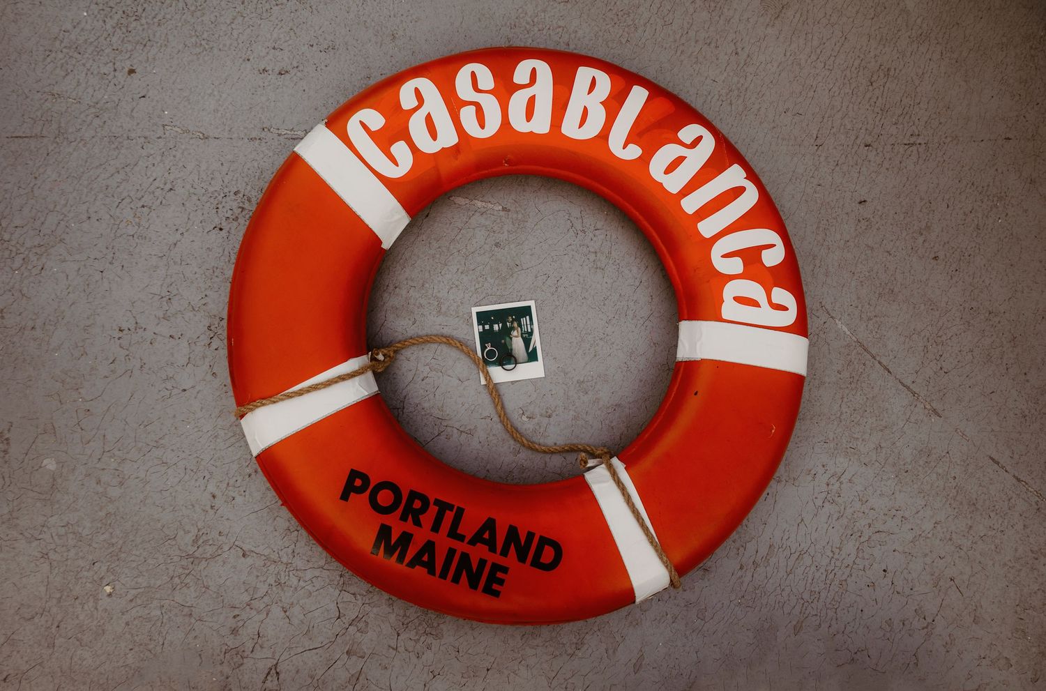 Orange and white life preserver ring labeled 'Casablanca' from Portland Maine mounted on a gray wall.