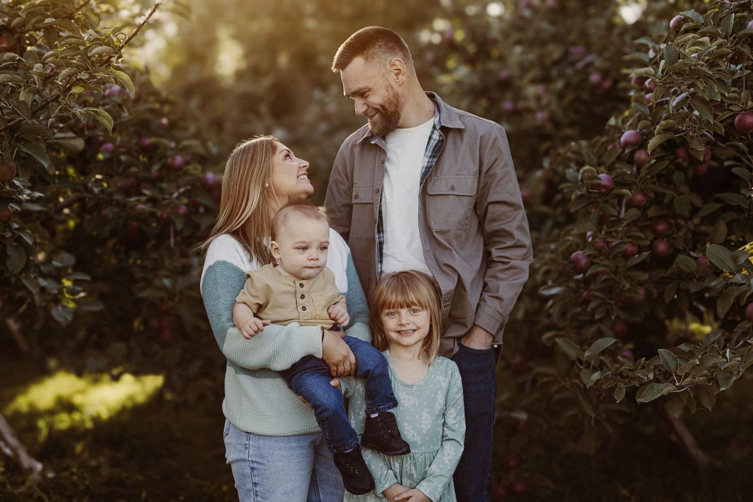 Family portrait amongst garden bushes during golden hour with soft natural lighting.