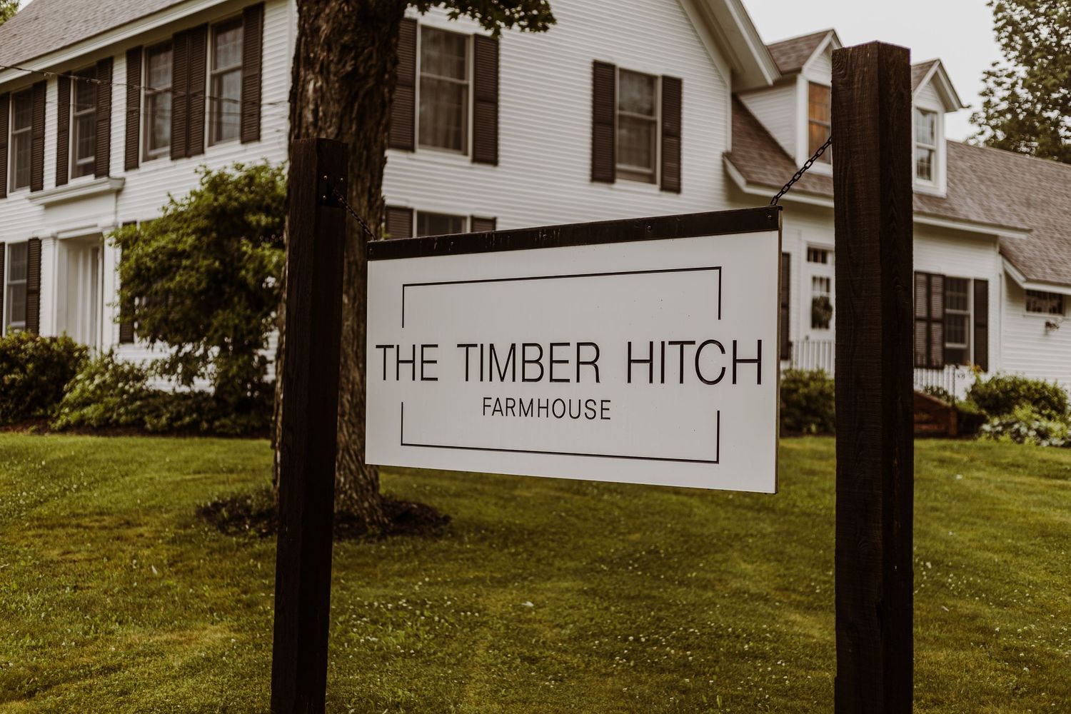 White farmhouse with 'The Timber Hitch' sign in front yard.