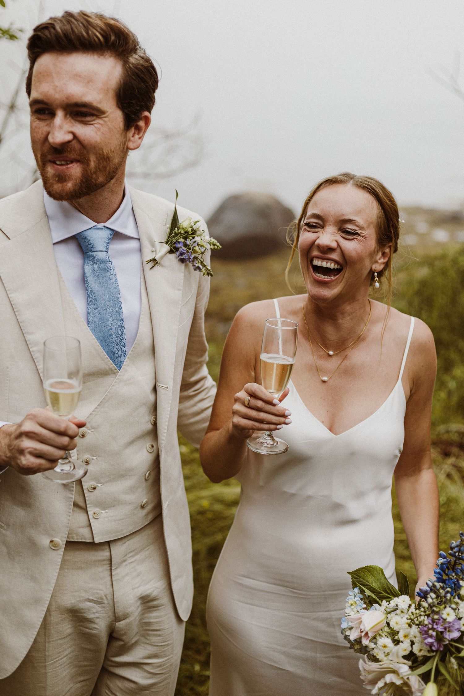 Wedding couple sharing champagne and laughter in garden setting.