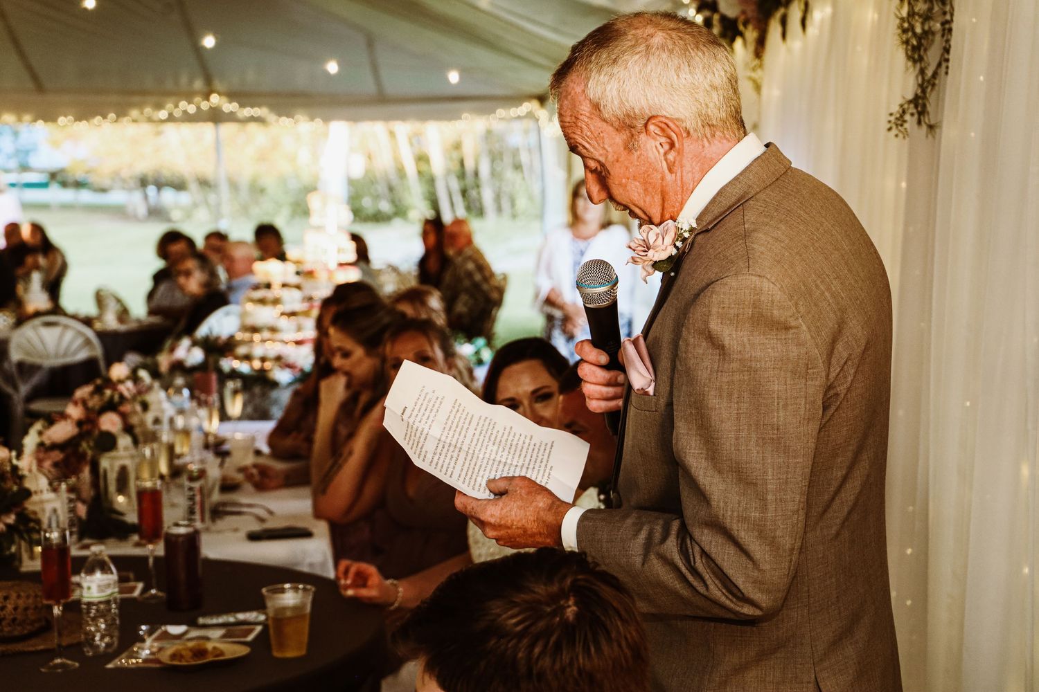 Speaker delivering speech at wedding reception under white tent.