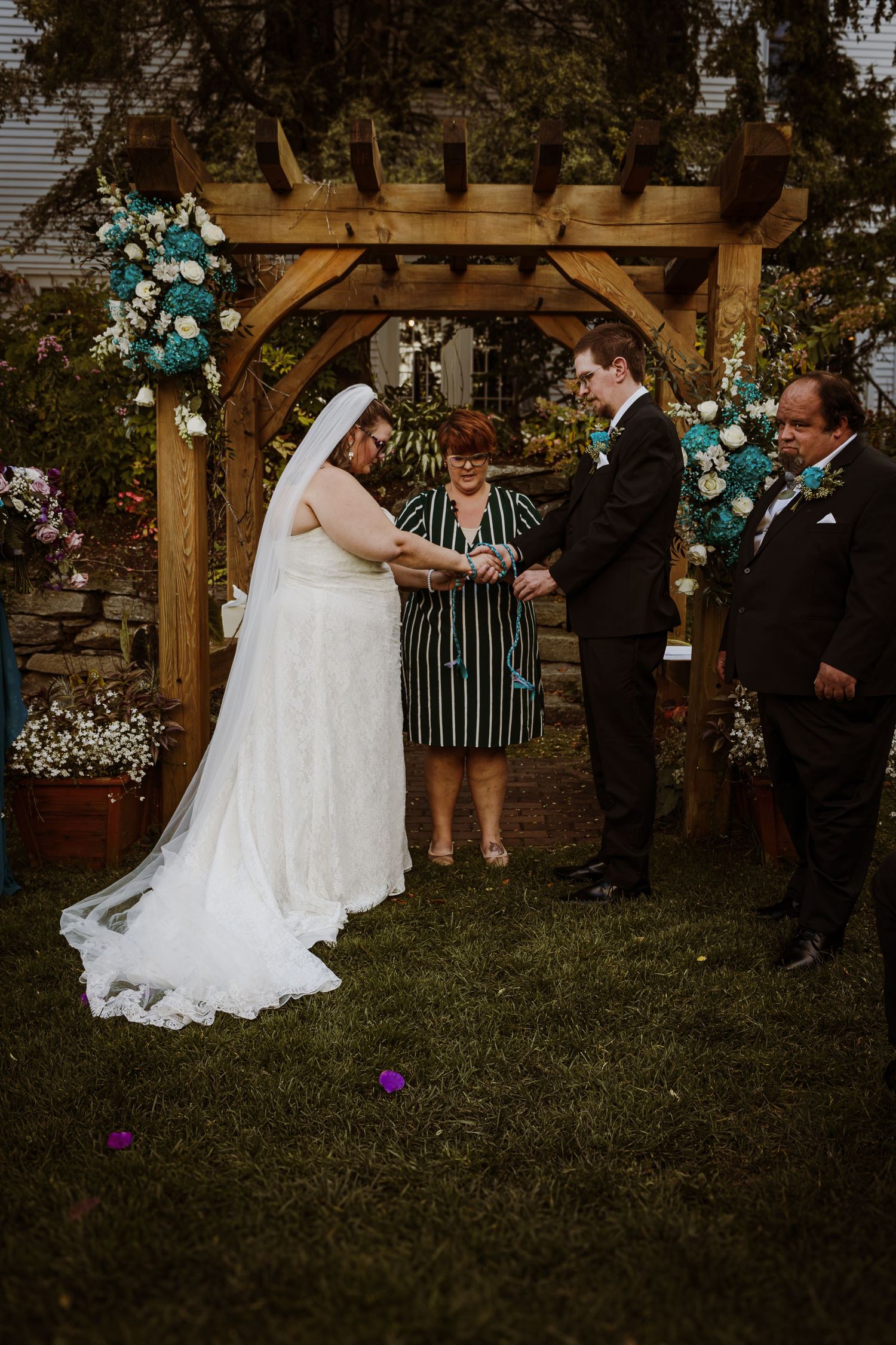 Outdoor wedding ceremony under a wooden arch decorated with blue and white flowers.