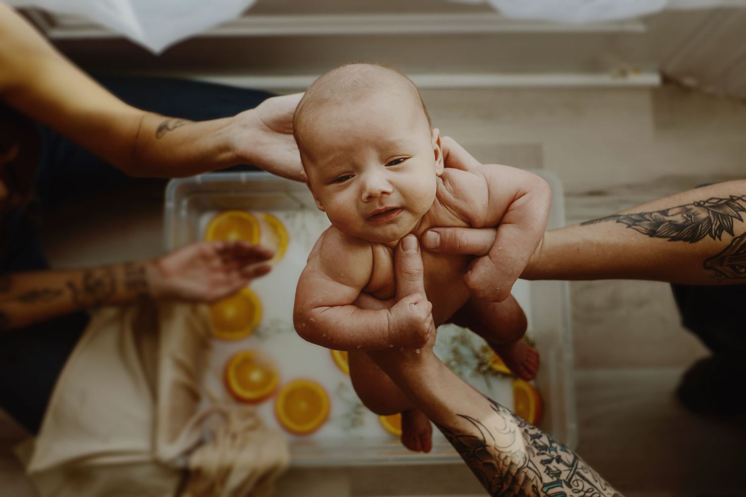 A gentle newborn bath ritual with orange slices and baby's breath flowers as natural decorative elements.