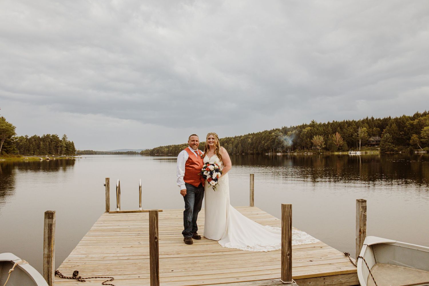 A couple shares a romantic moment on a lakeside dock surrounded by autumn trees.