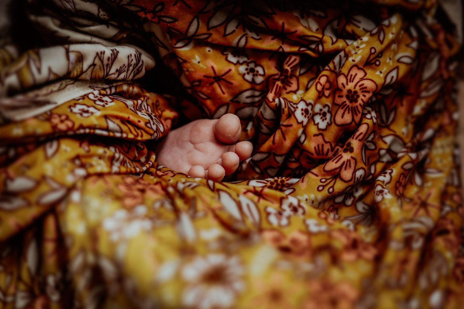 A small hand reaches out from beneath golden and orange patterned fabric.