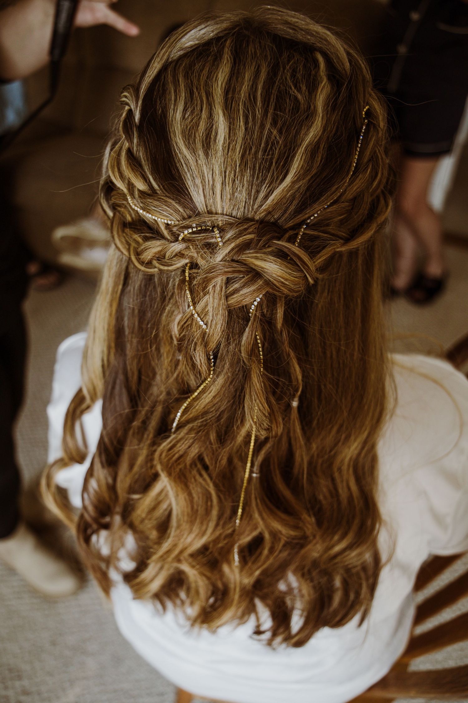 Intricately braided wedding hairstyle with loose curls and delicate details shown from behind.