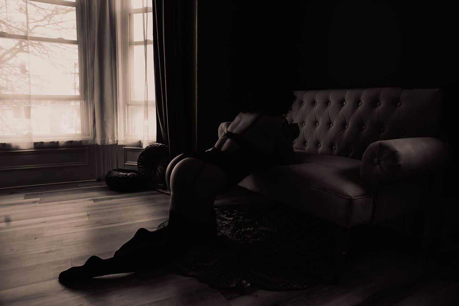 Silhouetted figure reclining on vintage sofa in shadowy room.