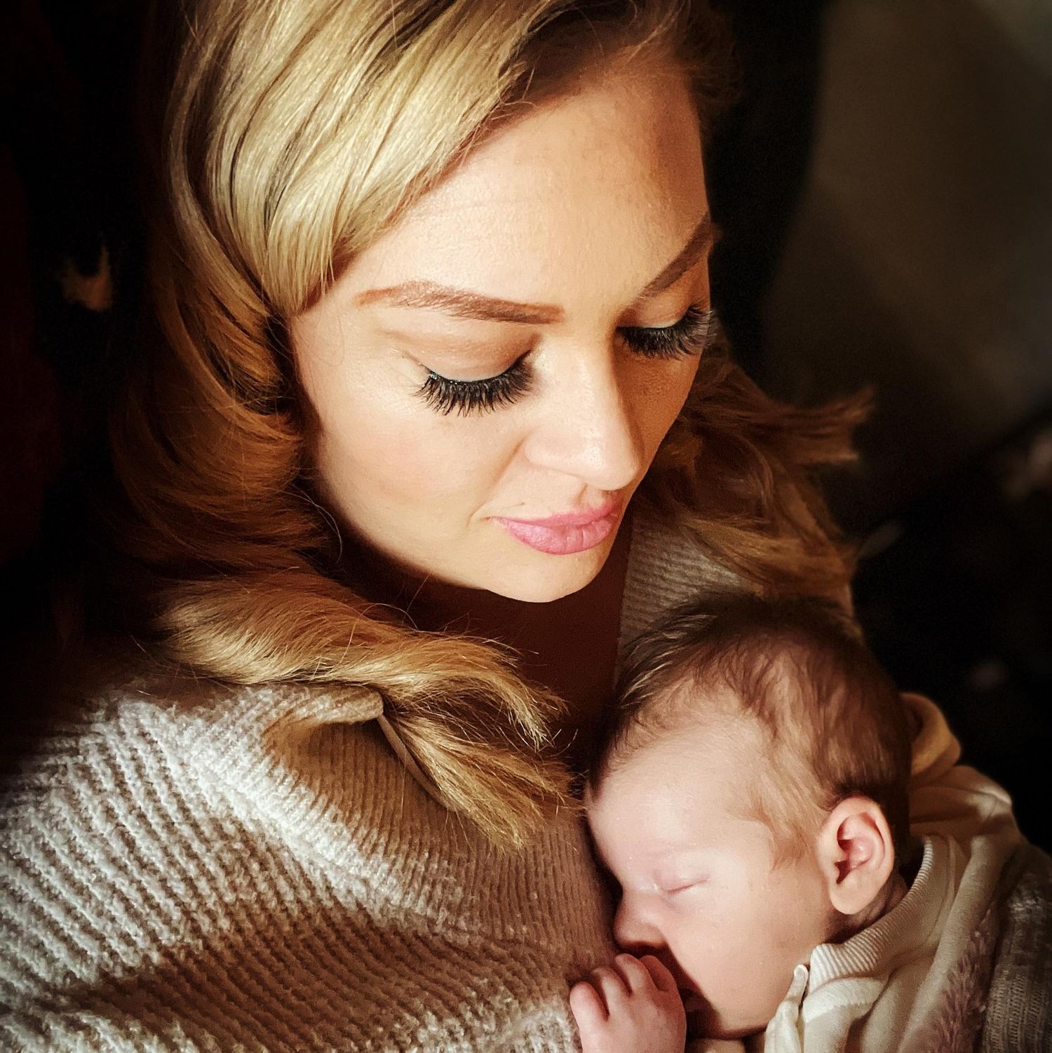 A tender moment captured between parent and sleeping infant in soft, warm lighting.