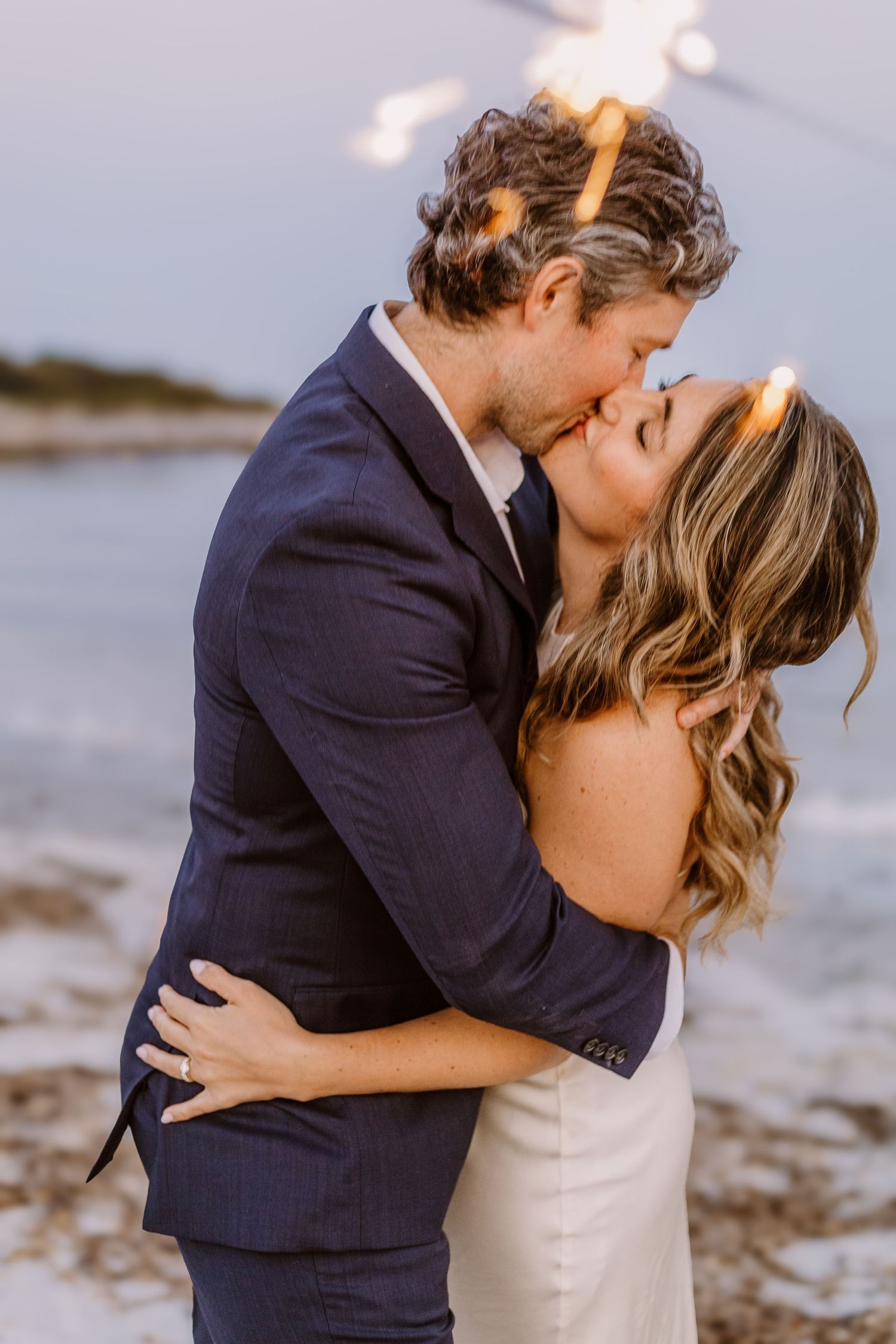 A romantic sunset kiss between newlyweds on a beach.