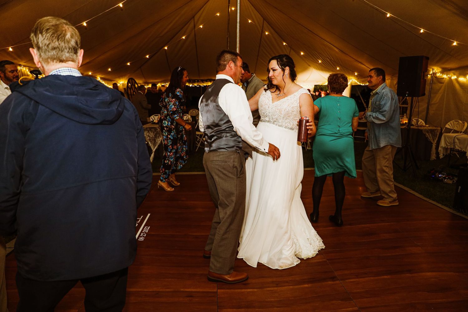 Couples dancing under a tent at a wedding reception with romantic lighting.