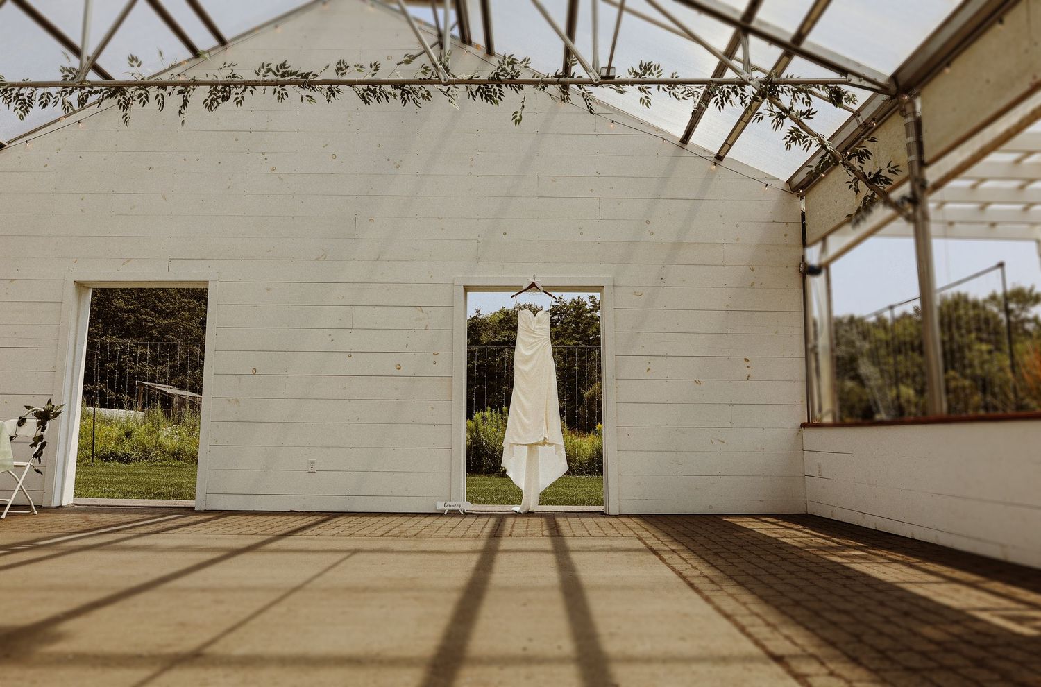 White wedding dress hanging in an elegant white barn venue with natural lighting.