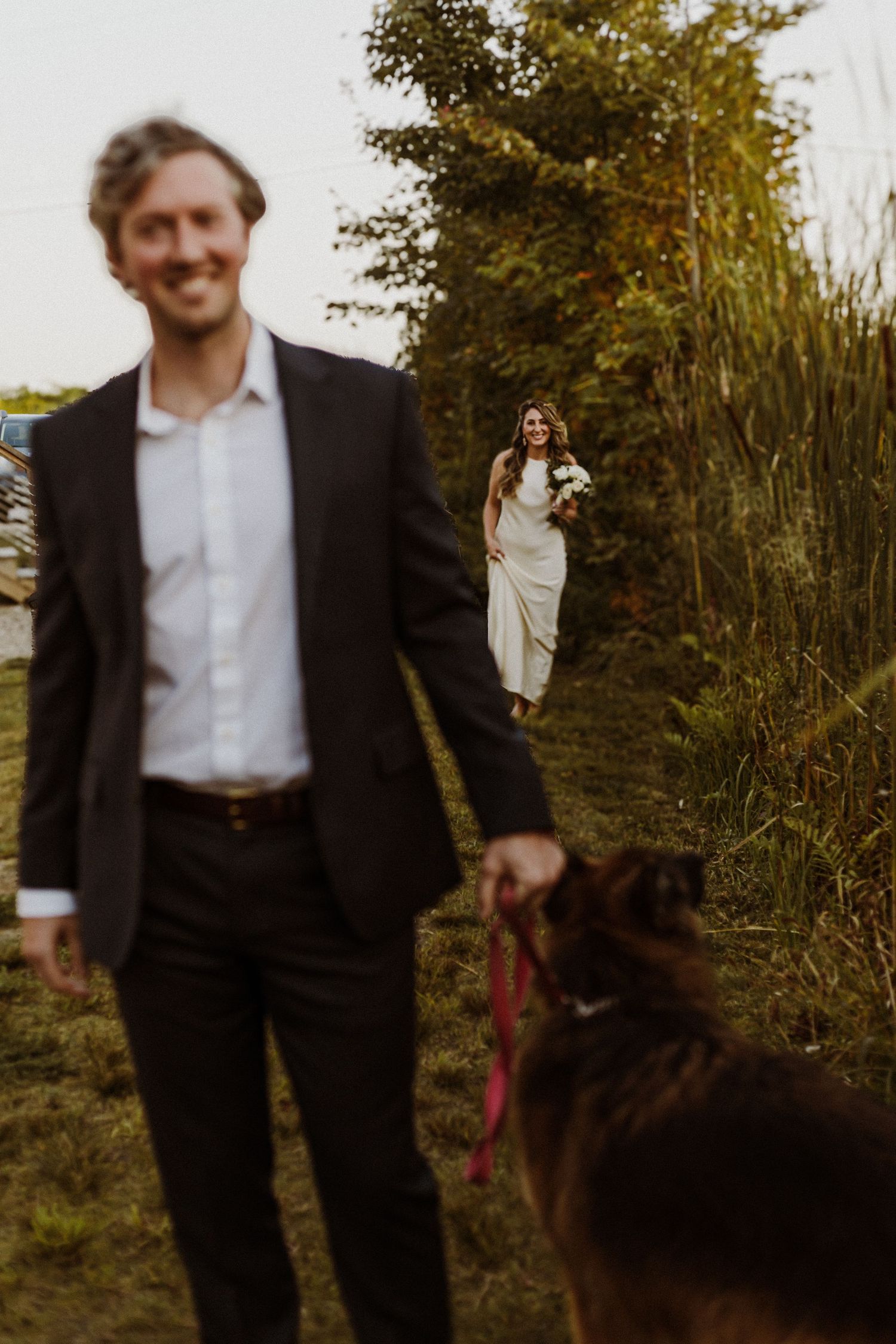 A scenic outdoor wedding moment with a dog on leash and natural foliage in the background.