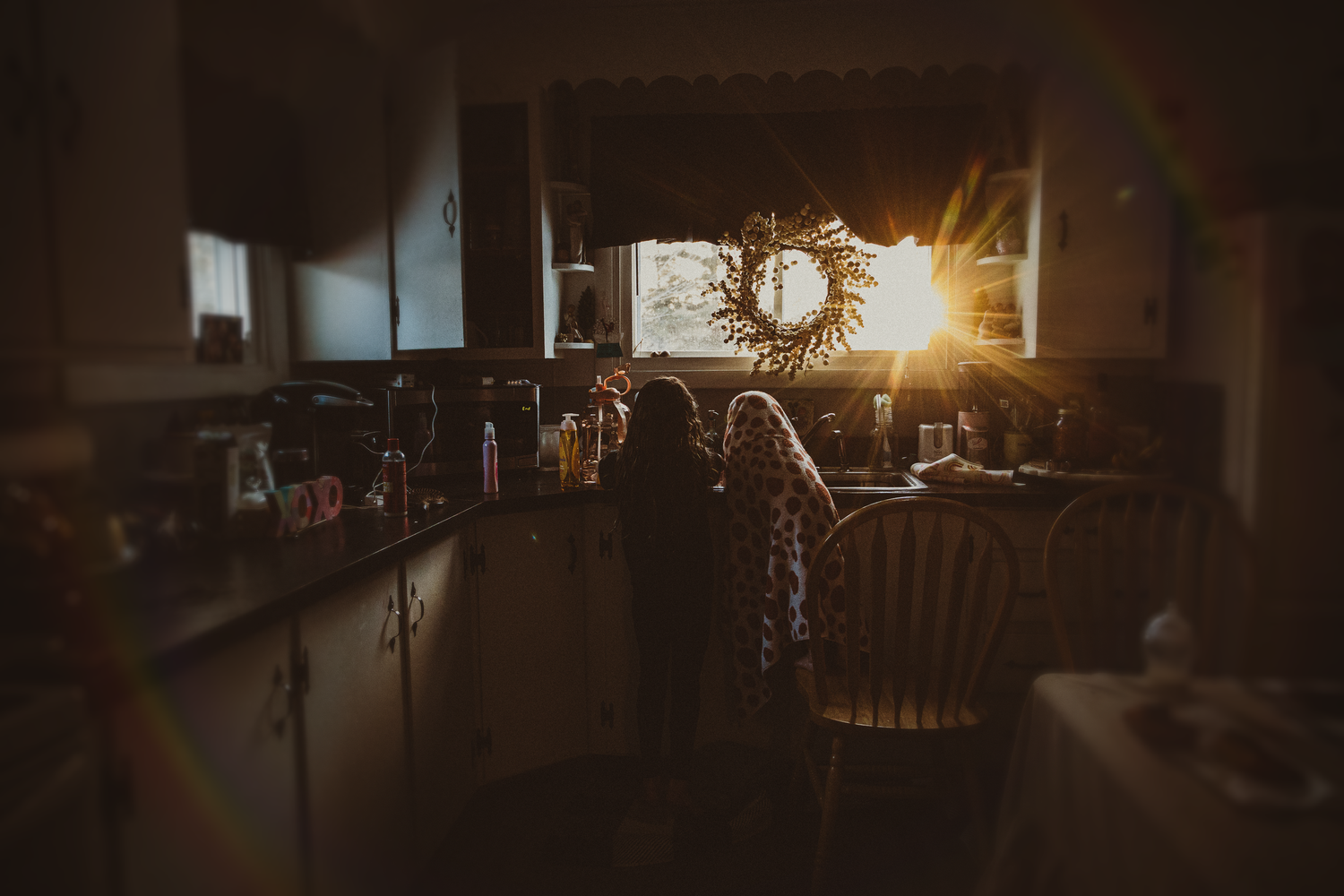 Silhouettes of people sitting at a dimly lit bar with sunlight streaming through window at golden hour.