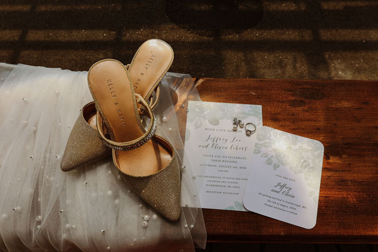 Wedding invitations and sparkly bridal shoes arranged on wooden surface.