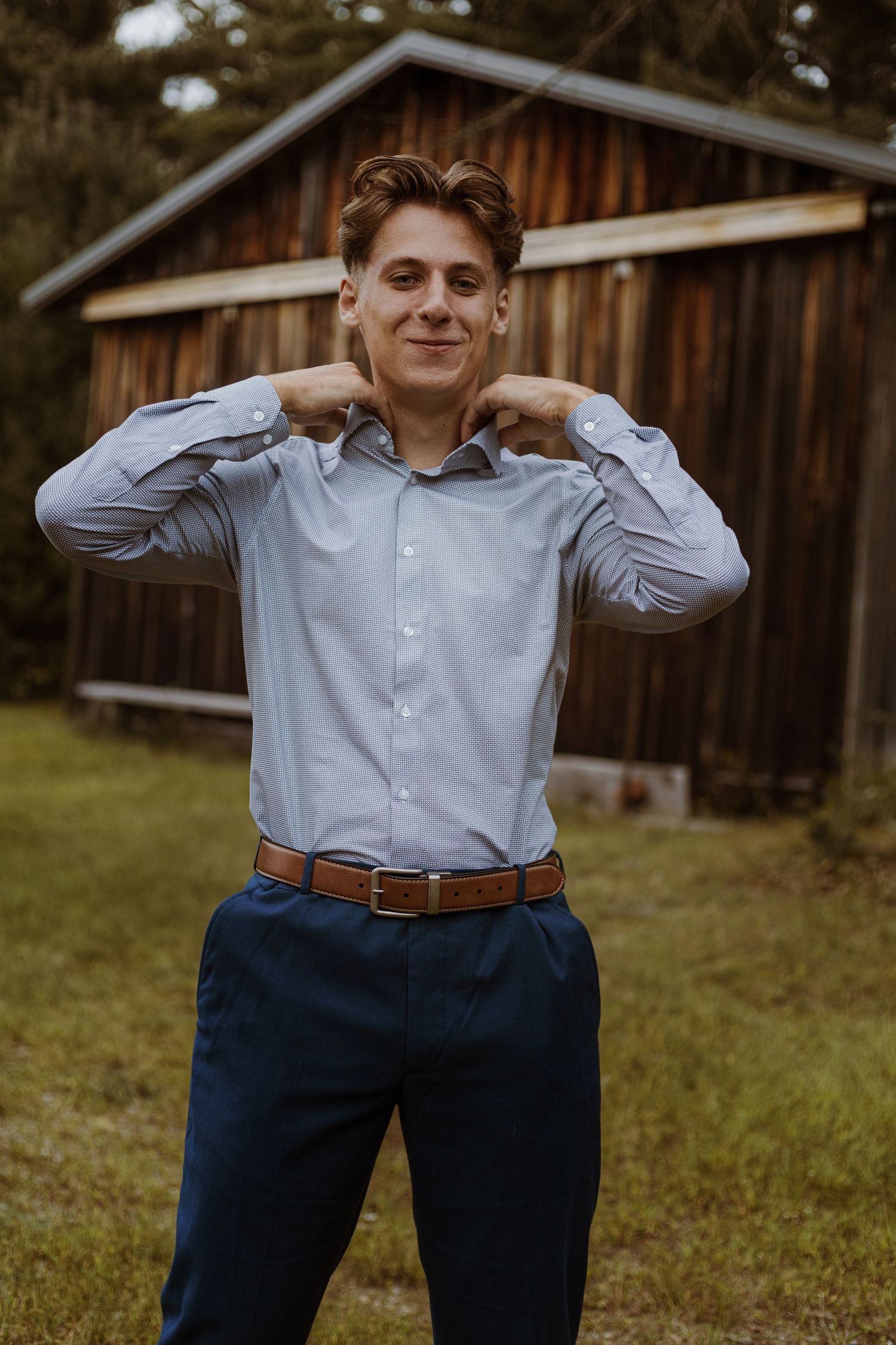 Casual portrait in front of wooden cabin wearing blue striped shirt and navy pants.