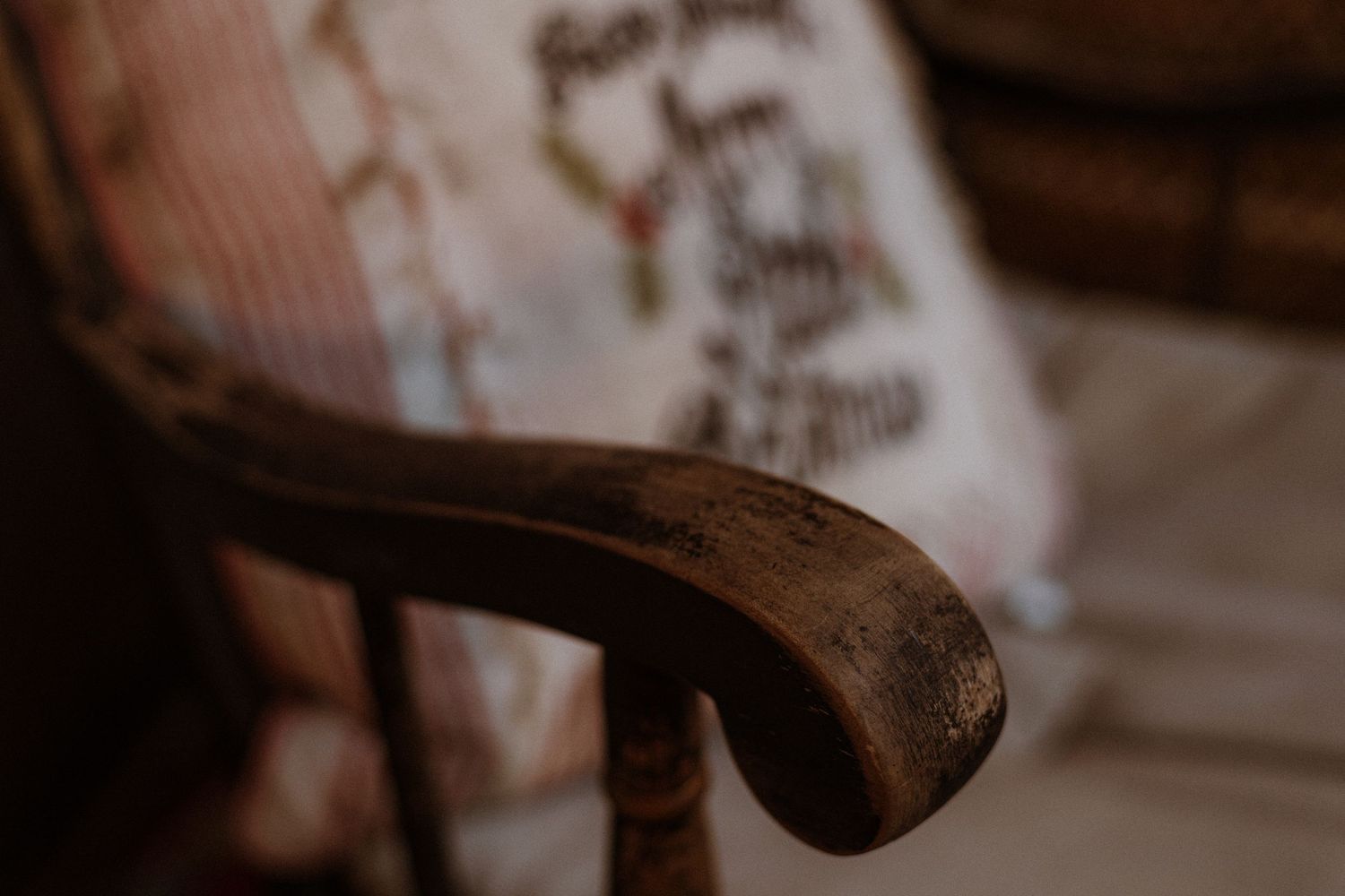 Macro shot of a dark wooden armrest detail on an antique chair in dramatic lighting.