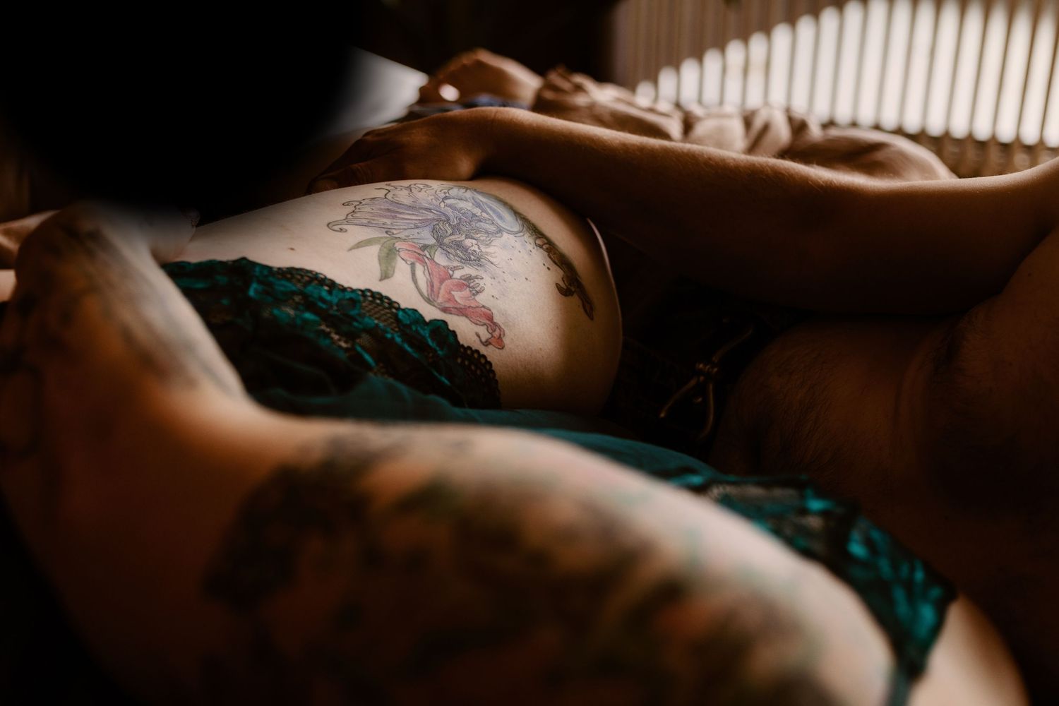 Close-up view of tattooed skin and green lace lingerie in moody lighting with soft shadows.