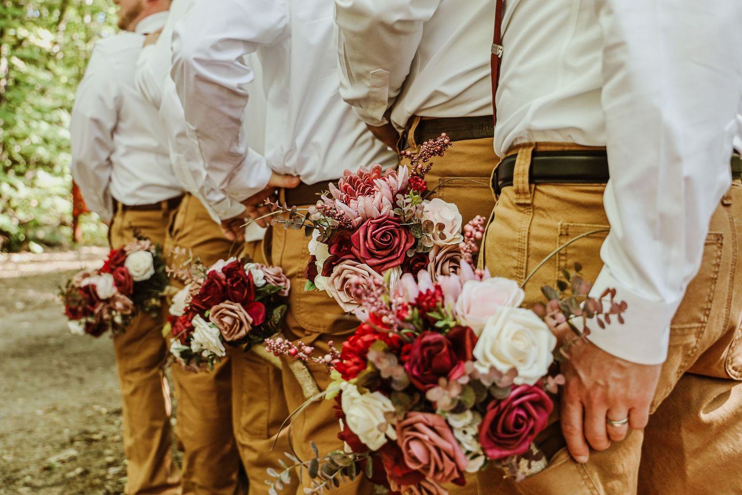 Groomsmen in khaki pants hold elegant burgundy and pink rose bouquets.