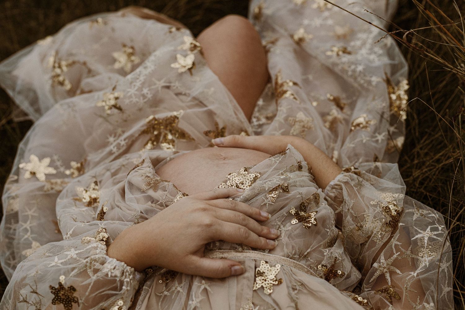 Delicate hands resting on ethereal tulle fabric adorned with golden sparkles and floral details.