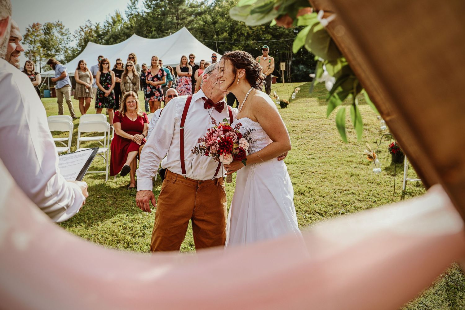Outdoor wedding ceremony with guests seated under a white tent.