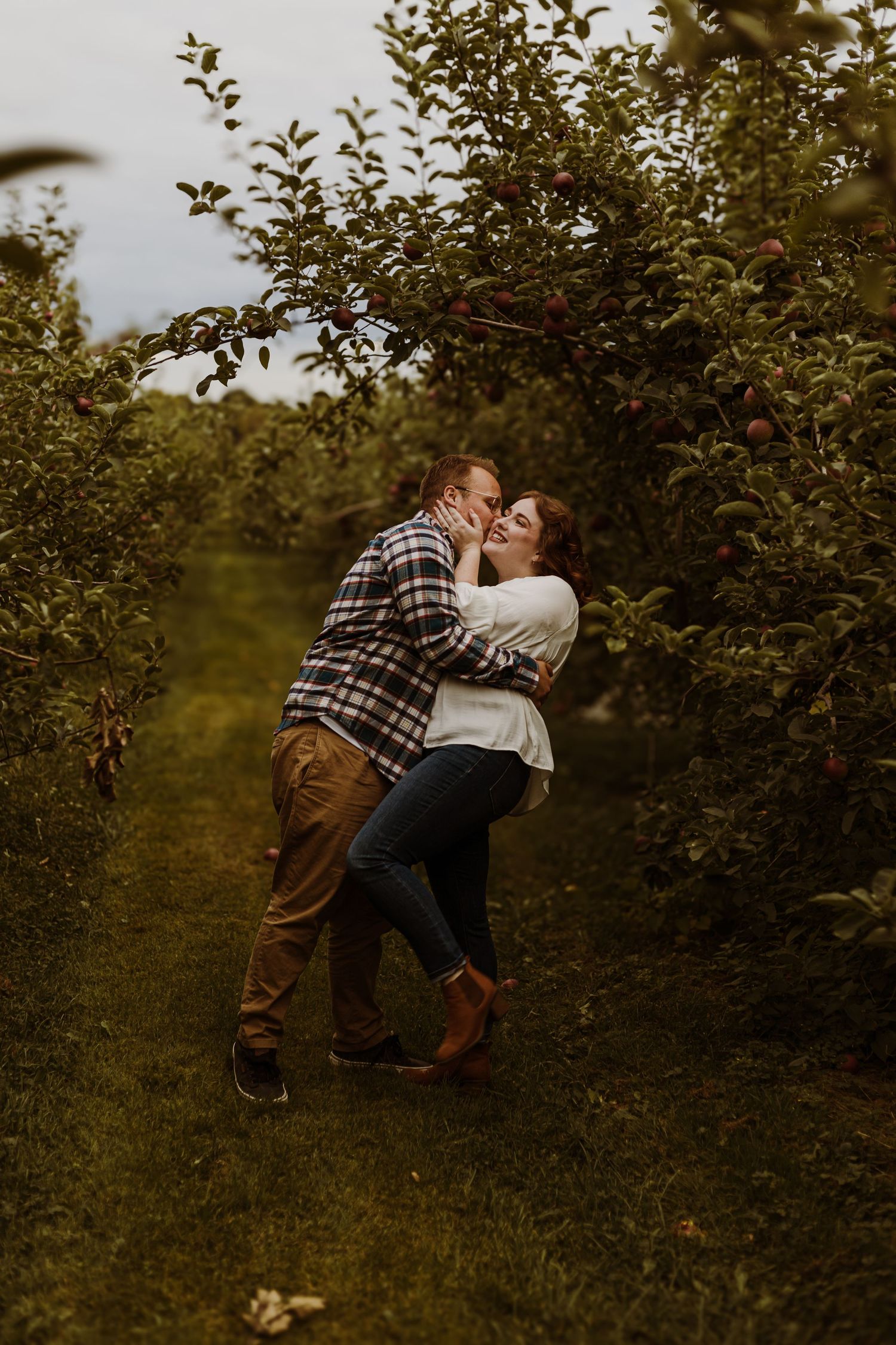 A couple sharing a romantic embrace among apple trees in an orchard during golden hour.