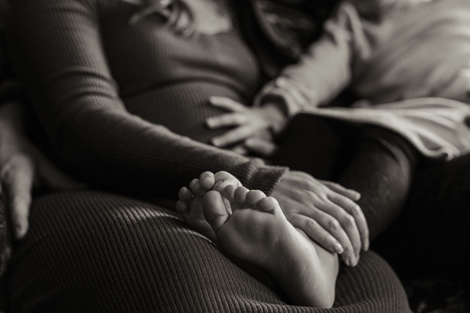 Black and white close-up of tiny baby feet resting on parent's hands.