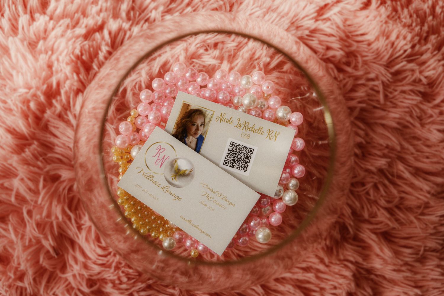 Business card and jewelry displayed on pink fuzzy texture background.
