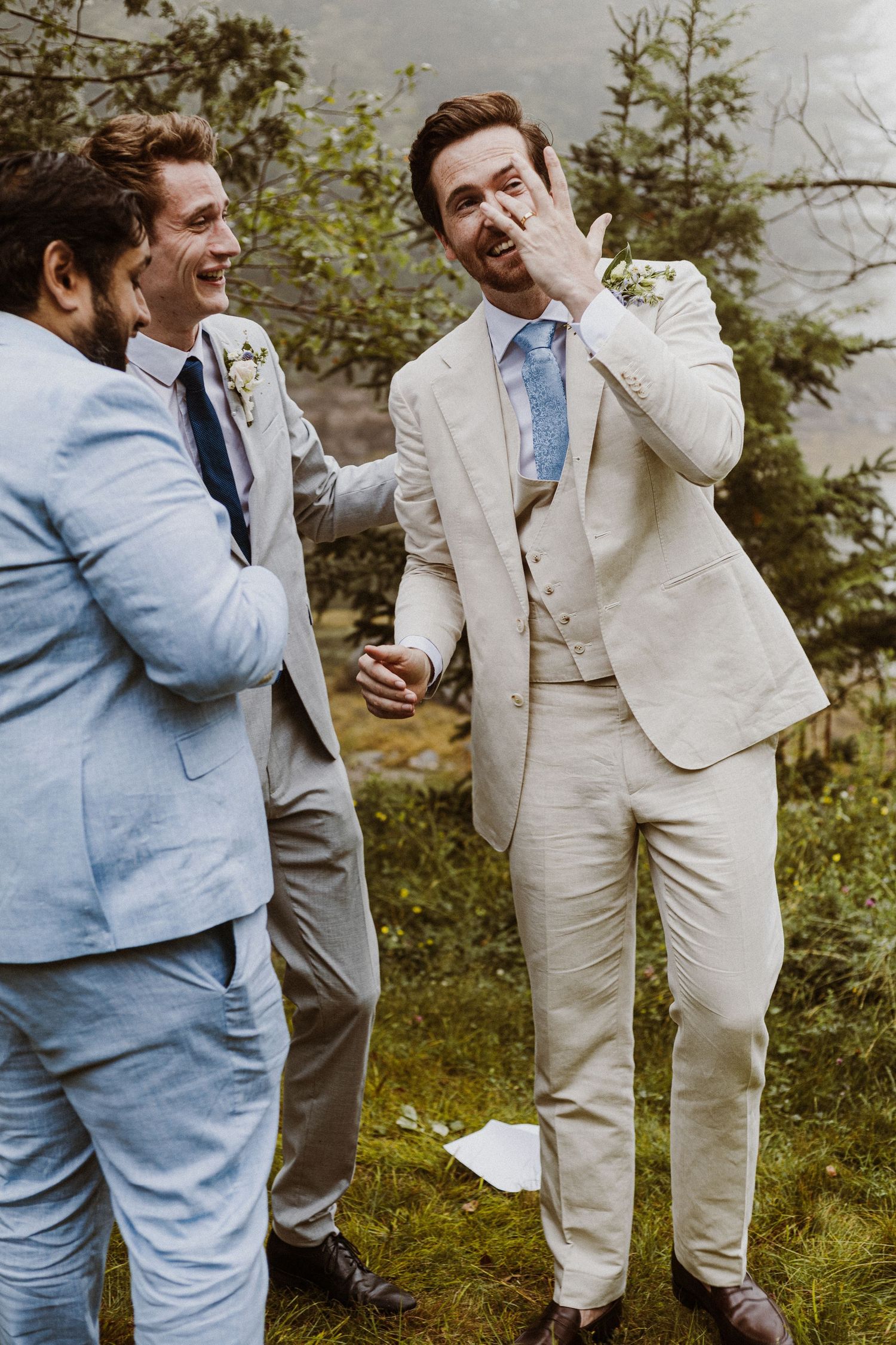 Groomsmen in light suits sharing a candid laughing moment outdoors.