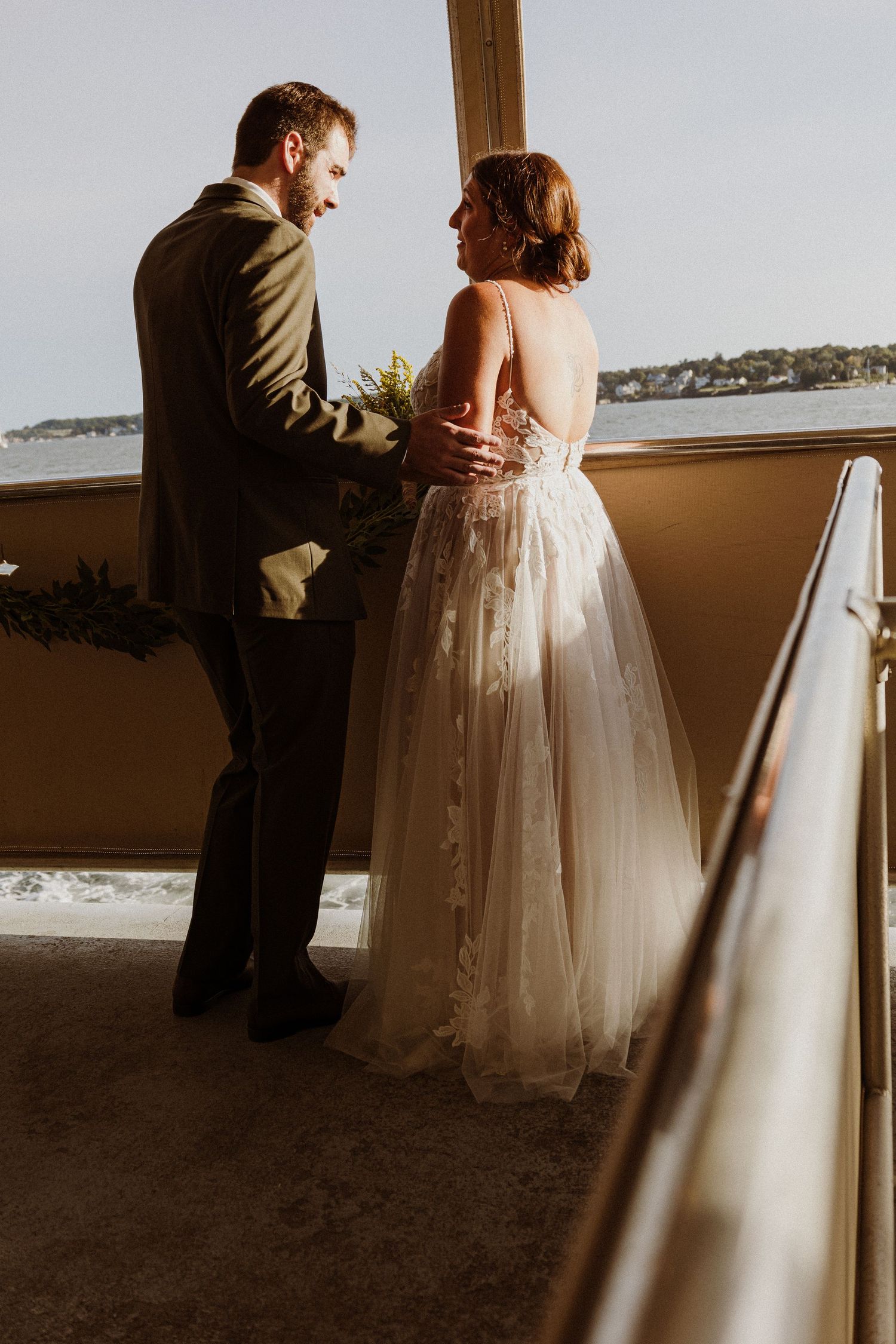Couple shares intimate moment in sunlit room overlooking harbor.