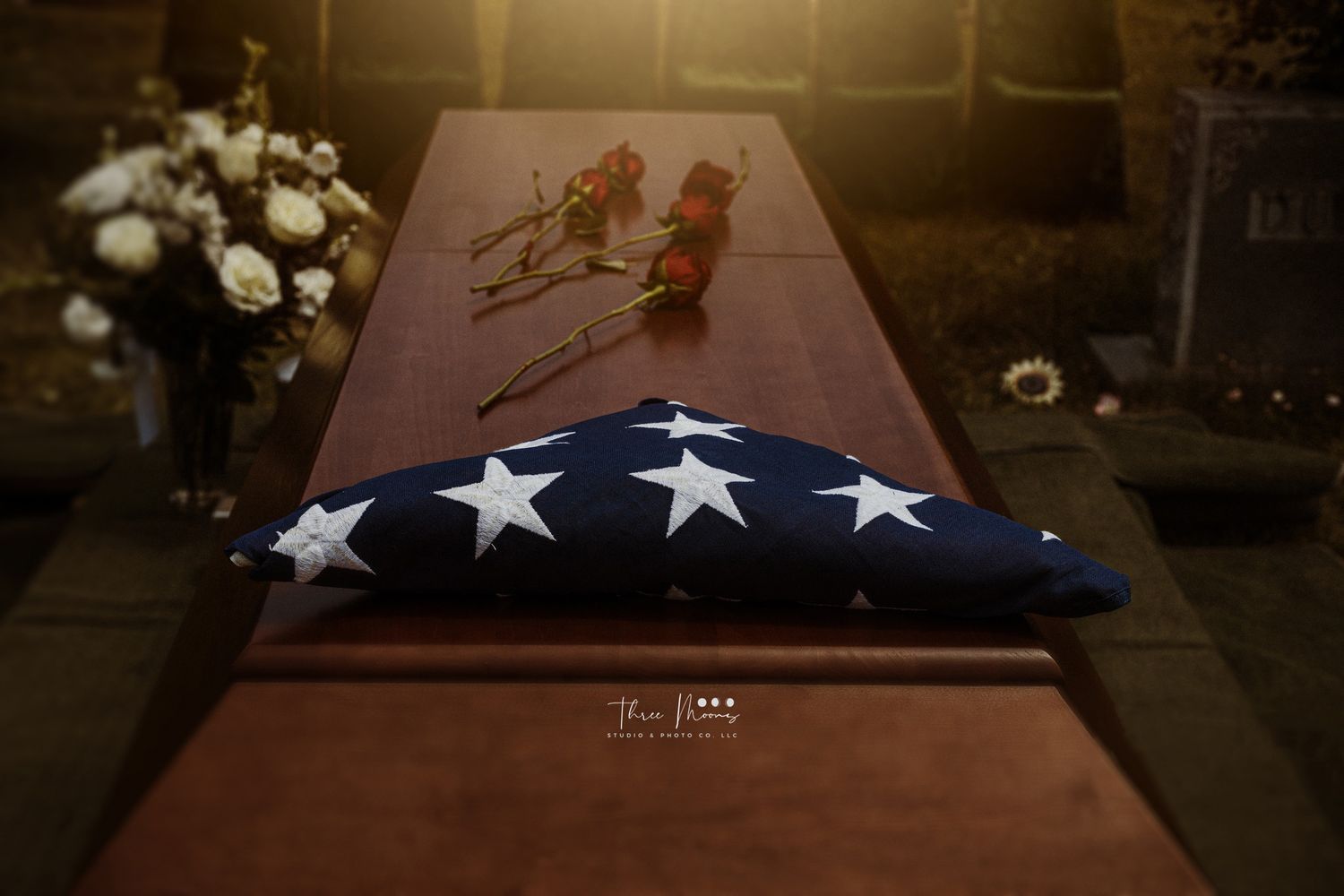 American flag folded in ceremonial triangle rests on wooden casket with flowers beside it during military funeral service.