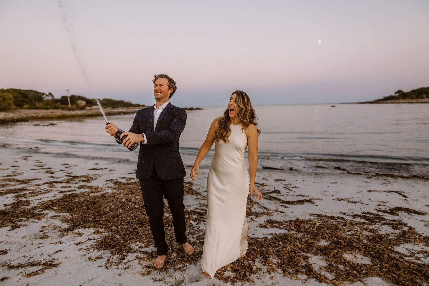 A couple celebrating on a beach at sunset with sparklers.