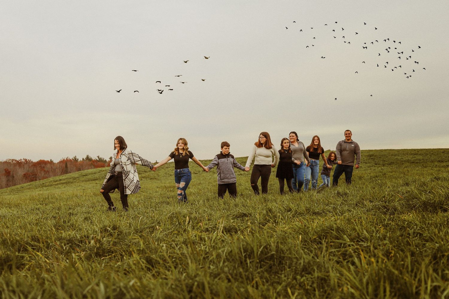 People run joyfully across a grassy hilltop with birds flying in the sky above.