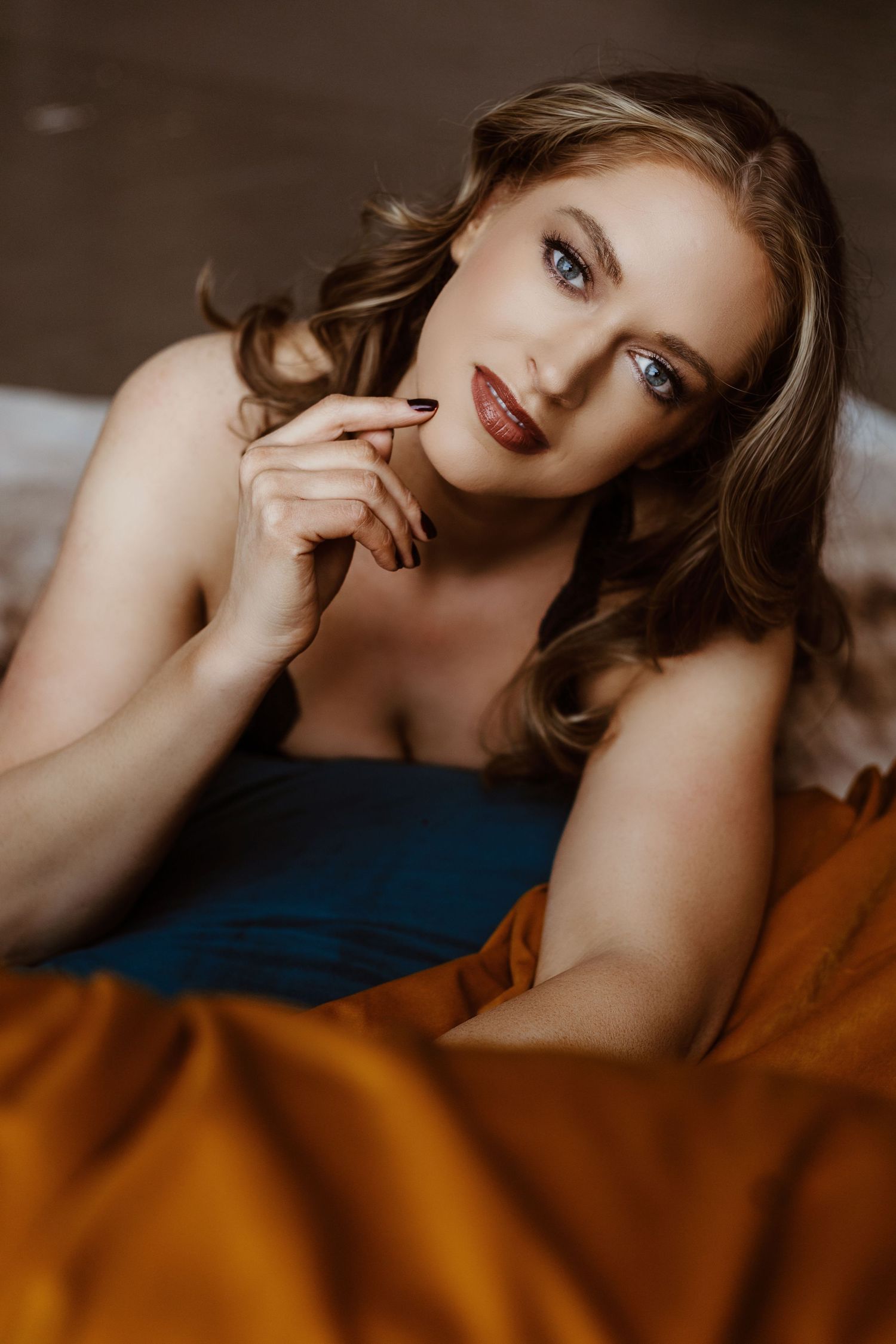 A boudoir portrait featuring soft lighting and warm earth-toned bedding.