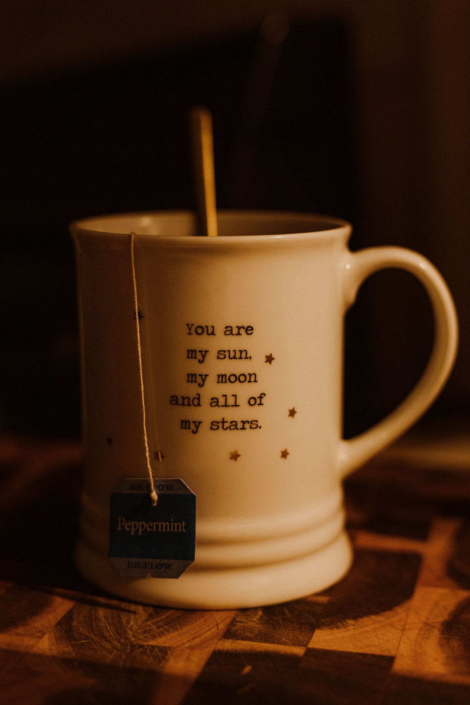 A white coffee mug with romantic text 'you are my sun, my moon and all of my stars' sits with a peppermint tea bag string.