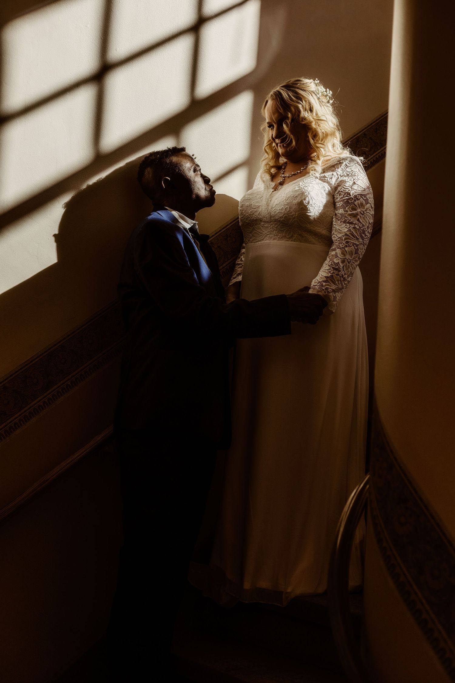 A romantic wedding photo showing a couple in dramatic window light on a staircase.