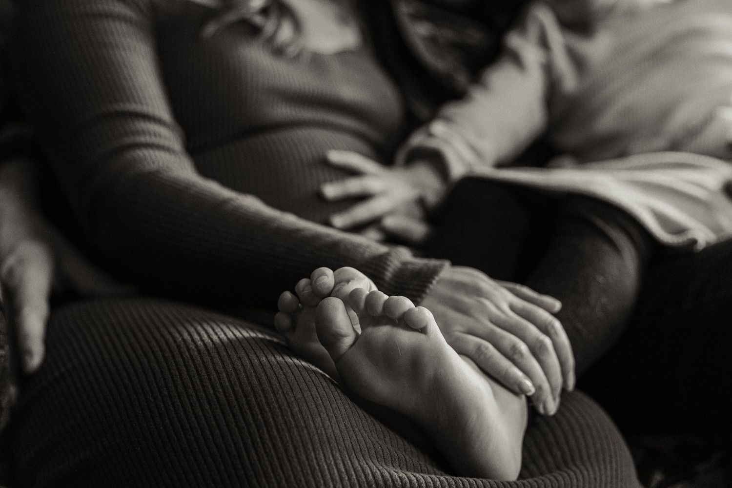 Black and white close-up of tiny baby feet resting on adult hands.