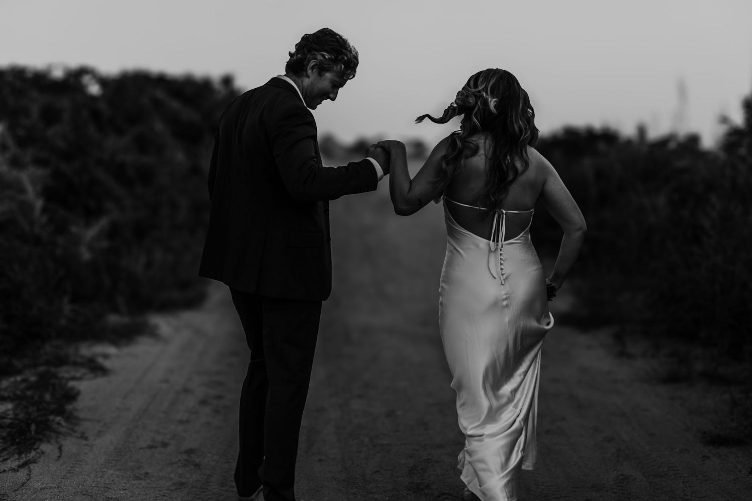 A black and white photo of a couple dancing on a rural path at dusk.
