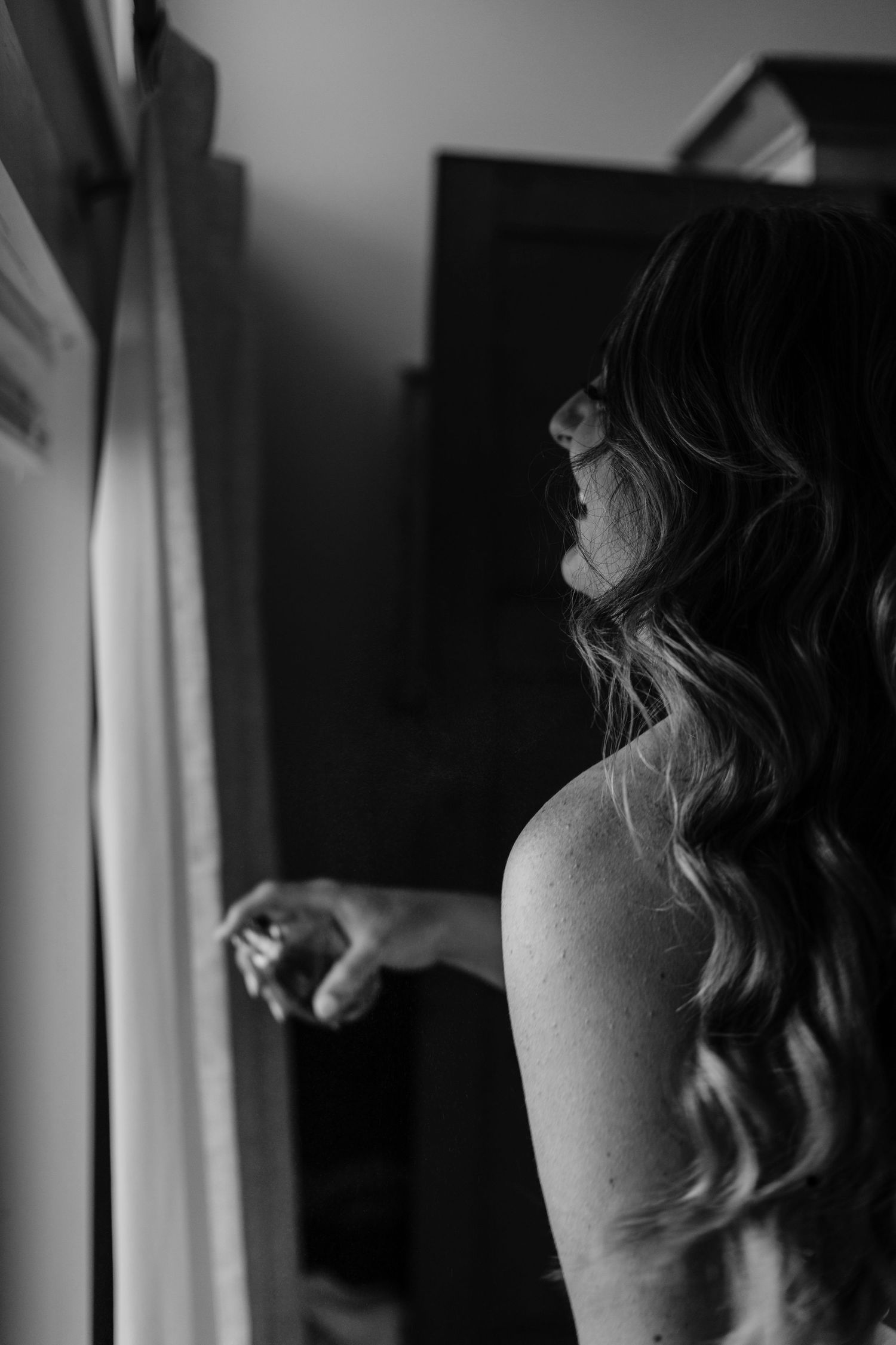 Silhouette by window showing long wavy hair and bare shoulder in dramatic light.