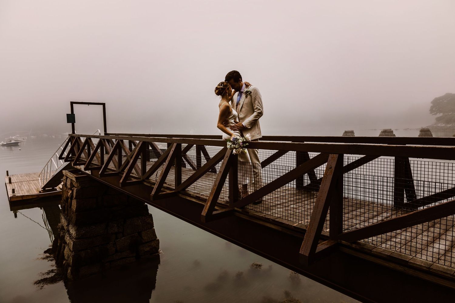 Romantic couple embracing on foggy dock overlooking misty water.