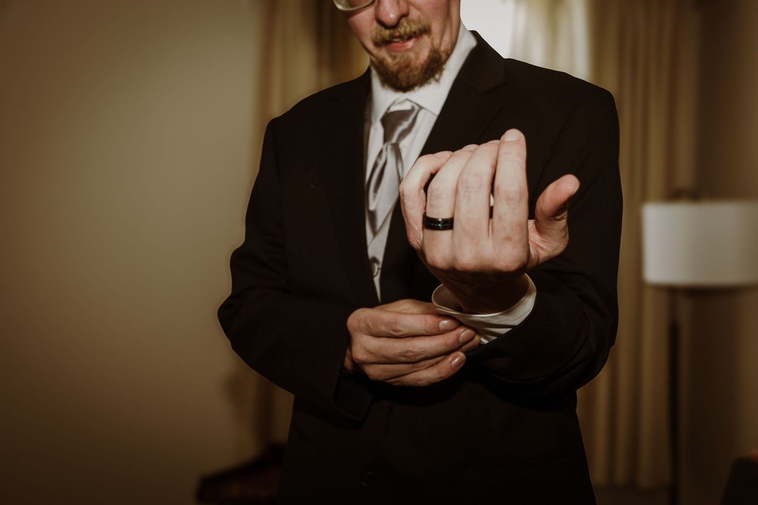 Close-up shot of hands adjusting cuff links on formal black suit.
