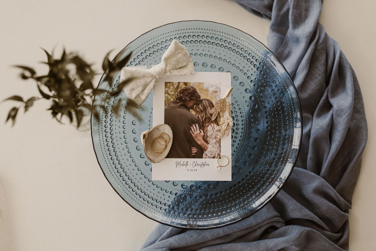 A vintage polaroid photo displayed on a textured blue glass plate with a cream colored bow and dried florals.